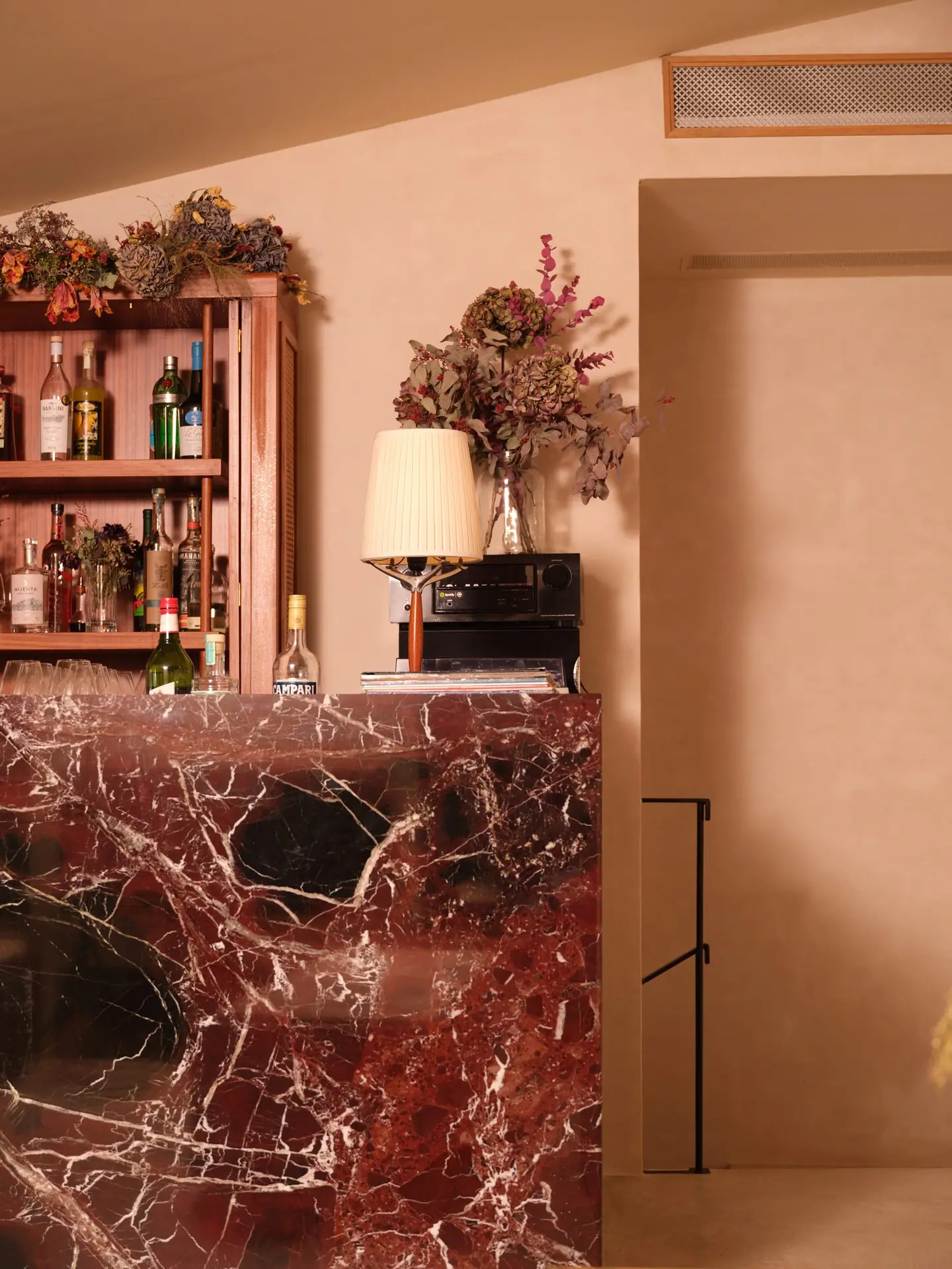 Comptoir bar en marbre rouge, étagère de spiritueux, fleurs séchées