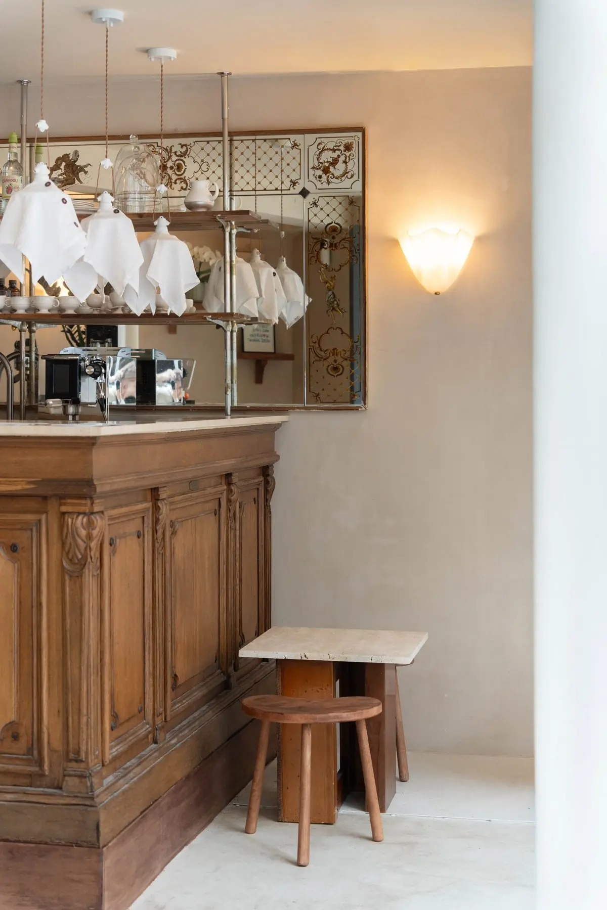 Comptoir en chêne sculpté, miroir doré gravé, suspensions en lin, guéridon en travertin et tabouret